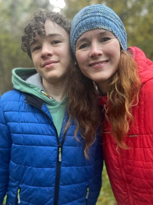 A boy and a girl posing for a photo in the woods.