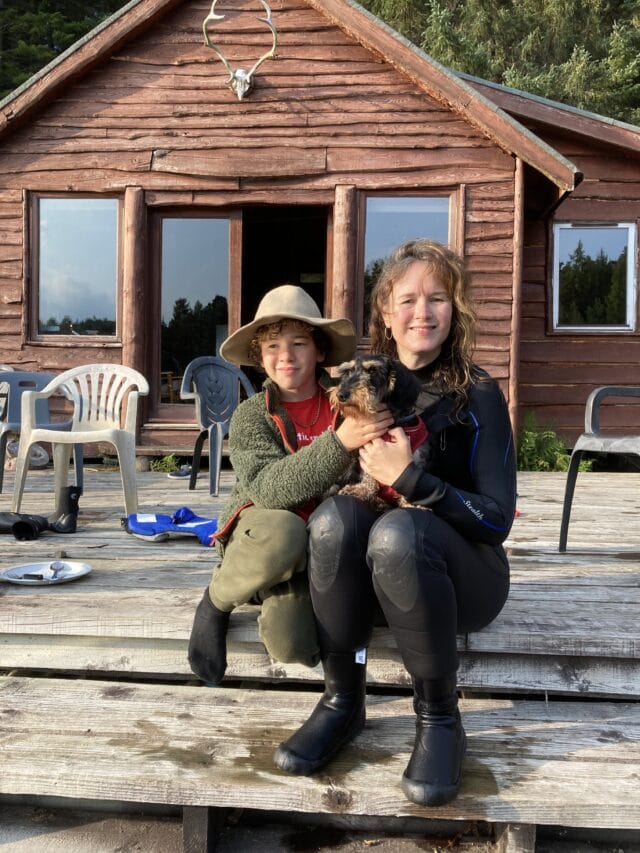 Two people sitting on the porch of a cabin with a dog.